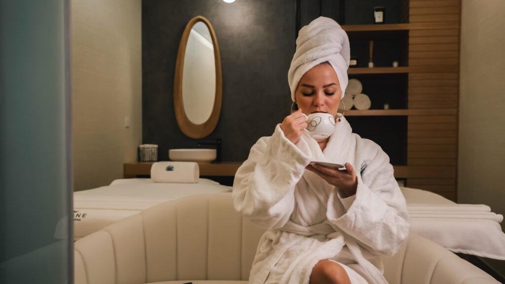 Woman in a comfy dressing gown and with towl on her head is enjoying a complimentary cup of coffee in a Swiss spa hotel