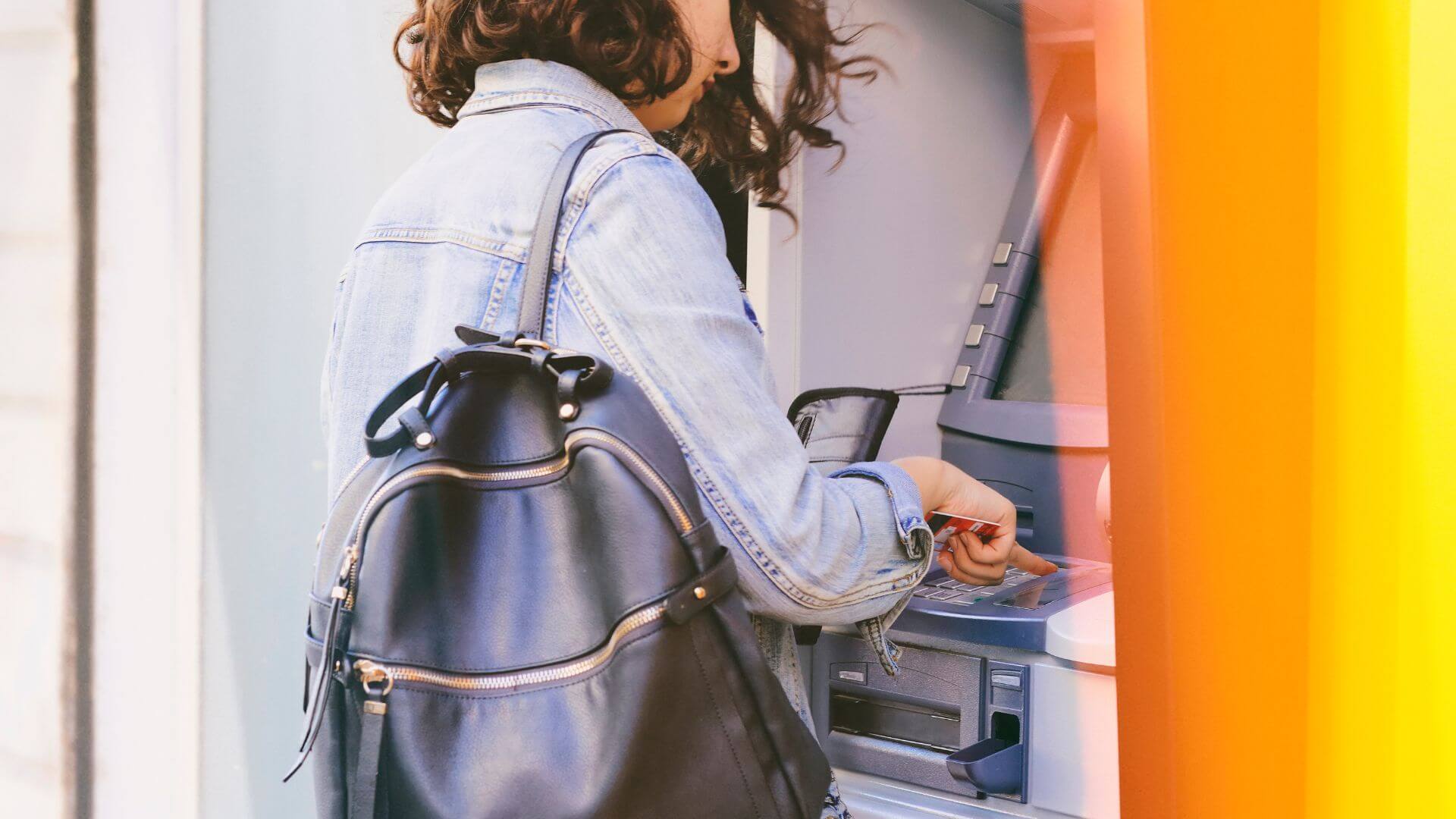 A woman with a backpack is using an ATM on her tour to Europe