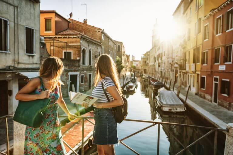 Two women on a bridge in Venice. One of them is holding a travel guide.