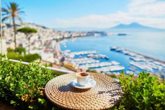 A cup of espresso on a table in a Naples cafe. Beautiful coastline and Vesuveus are visible on the background.
