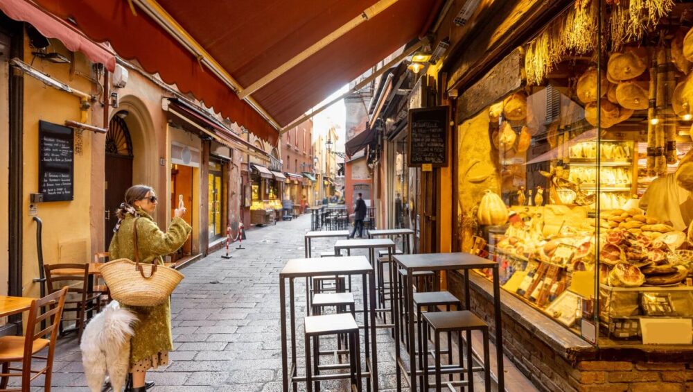 A woman near a food store in Bologna, a must-visit destination on a food tour to Italy